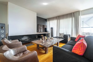 A modern living room with a fireplace, black and brown leather sofas, a wooden coffee table, and a large window with curtains. - K&K Villa in Athens Riviera with private pool (Voula)