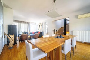 A modern living room with a wooden dining table, white chairs, a sofa, and a staircase. - K&K Villa in Athens Riviera with private pool (Voula)