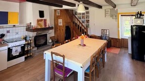 A kitchen with a dining table, wooden beams, a stove, and a refrigerator. - Le Maguero (Guégon)