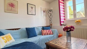 A cozy room with a sofa, a table, and a window with striped curtains. - Le Maguero (Guégon)