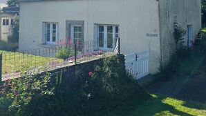 A two-story house with a sloped roof, a chimney, and a small garden with flowers. - Le Maguero (Guégon)