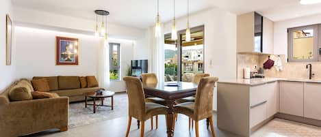 A modern living room with a sofa, dining table, and chairs, a kitchen with a sink and cabinets, and a large window with a view.