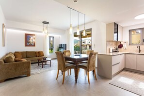 A modern living room with a sofa, dining table, and chairs, a kitchen with a sink and cabinets, and a large window with a view. - Urban Panorama - Stylish Stay in Kalamata (Kalamata)