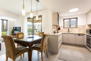 A modern kitchen with a dining area, large windows, and a view of buildings. - Urban Panorama - Stylish Stay in Kalamata (Kalamata)