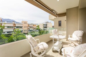 A balcony with white rocking chairs and a table, overlooking a residential area with buildings and greenery. - Urban Panorama - Stylish Stay in Kalamata (Kalamata)