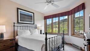 A bedroom with a bed, a nightstand, a lamp, a ceiling fan, and large windows with a view of greenery. - Beaver Creek Ski-In/Ski-Out w/Mountain View|UB308 (Beaver Creek)