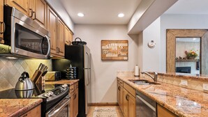 A kitchen with wooden cabinets, stainless steel appliances, a granite countertop, and a patterned rug. - Beaver Creek Ski-In/Ski-Out w/Mountain View|UB308 (Beaver Creek)
