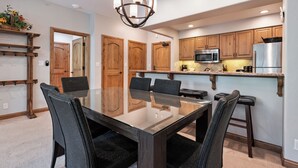 A modern kitchen with wooden cabinets, a stainless steel refrigerator, a microwave, and a glass dining table with chairs. - Beaver Creek Ski-In/Ski-Out w/Mountain View|UB308 (Beaver Creek)
