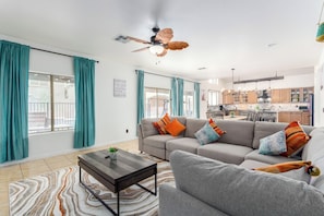 A modern living room with a sofa, coffee table, and a ceiling fan. - Cactus House: 5BR Family Fun Hub (Avondale)