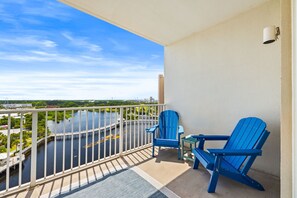A balcony with a view of a river, two blue chairs, and a small table. - Laketown Luxury| Unit 935| Fully Renovated (Panama City Beach)