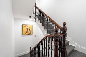 Eine Treppe mit Holzgeländer und schwarzen Spindeln, ein gelistet Rahmenkunstwerk an der Wand und ein Rauchverbot-Schild.