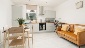 A modern kitchen with white cabinets, a dining area with wooden chairs, and a brown leather sofa. - 3 Desks & 4 TVs | Flex Bed Config | Secure Parking (Merseyside)