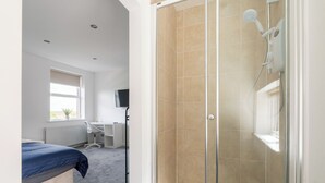 A bedroom with a bed, a desk, a chair, a shower with glass doors, and a window. - 3 Desks & 4 TVs | Flex Bed Config | Secure Parking (Merseyside)