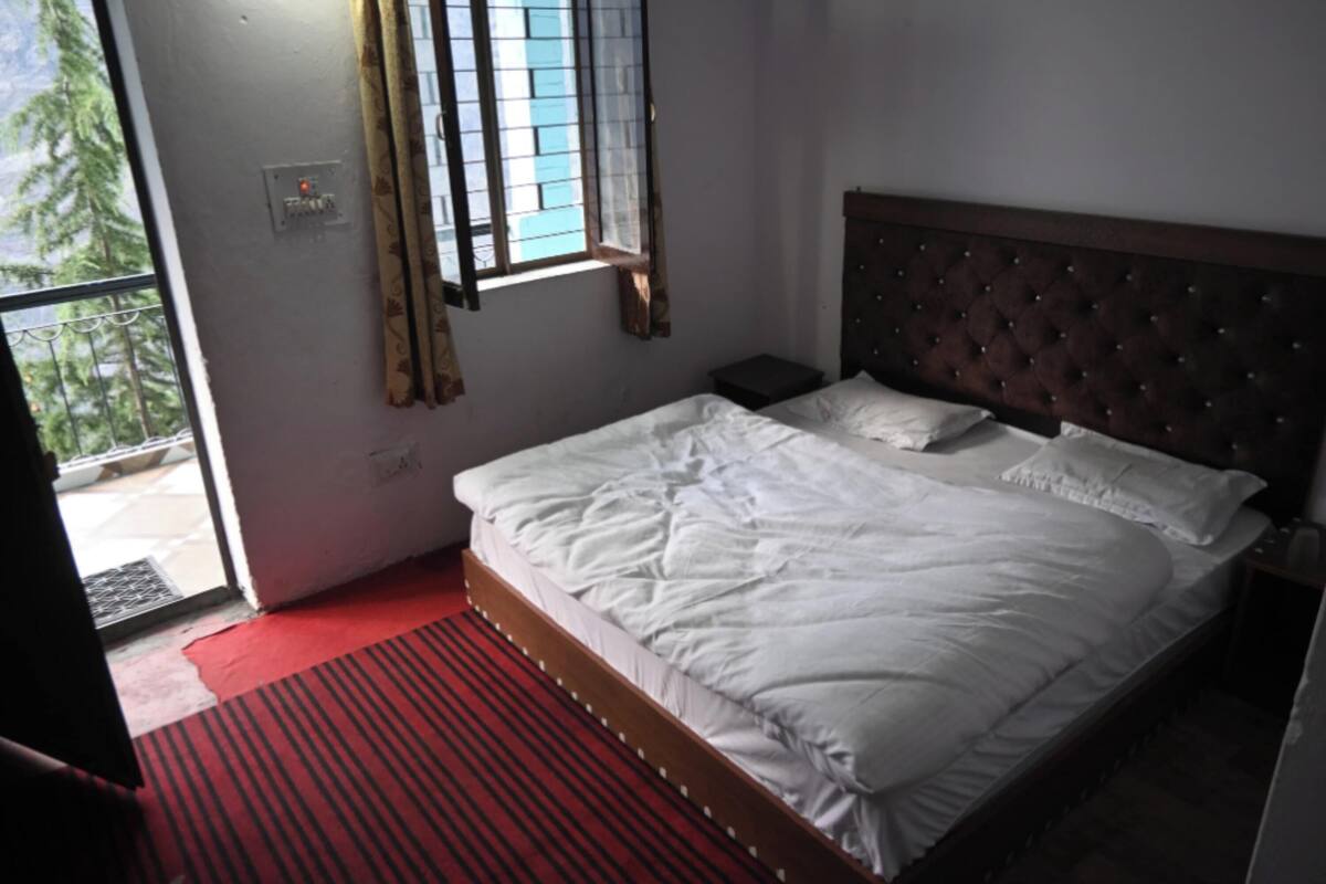 A bedroom with a bed, a nightstand, a window with curtains, and a red carpet.