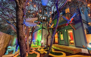Ein Baumhaus mit Wendeltreppe, umgeben von Bäumen und beleuchtet mit Lichterketten.