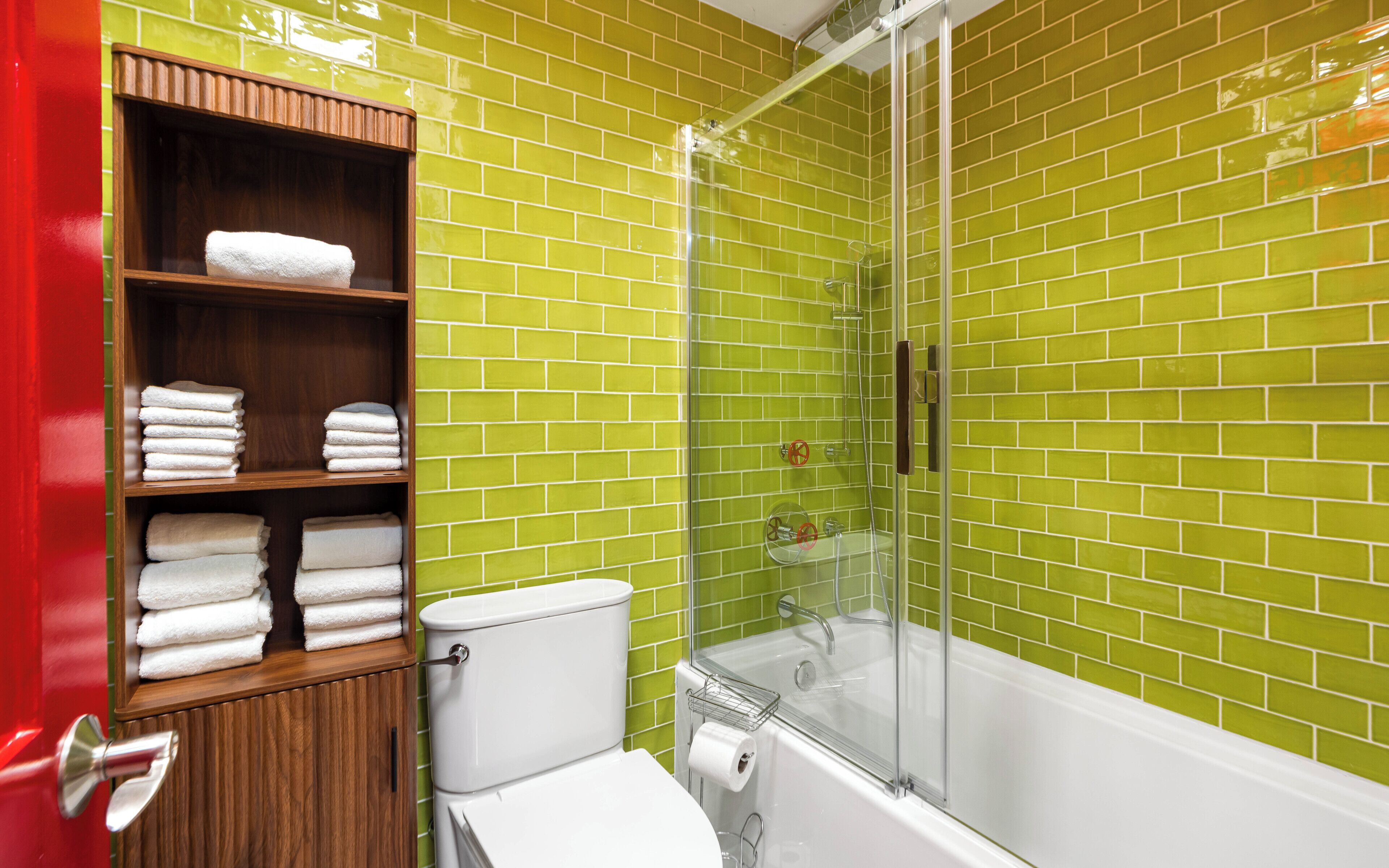 A bathroom with a toilet, a shower with a glass door, and a shelf with towels.