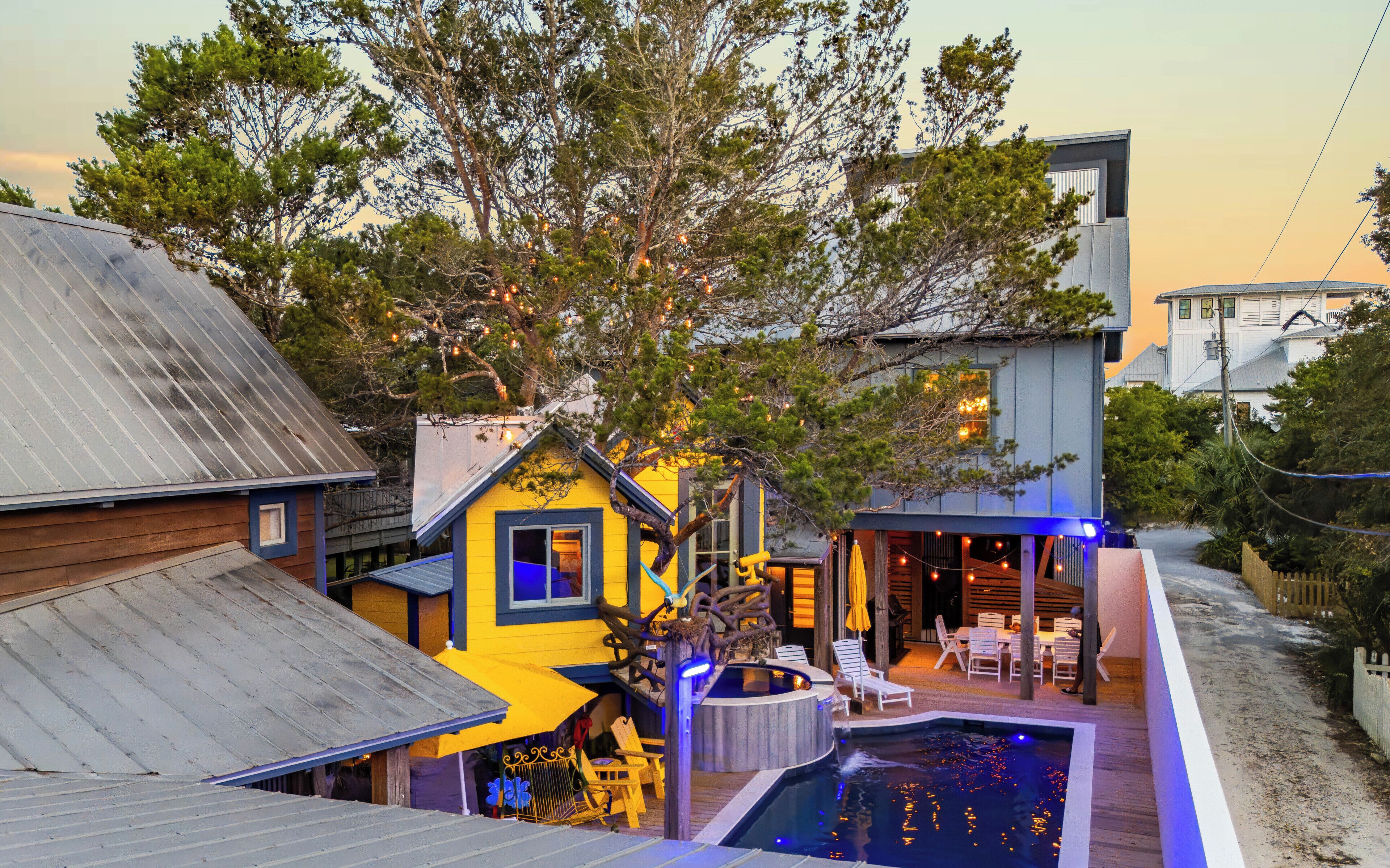 A residential property with a swimming pool, outdoor seating, and a large tree.