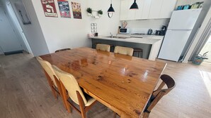 A wooden dining table with chairs, a kitchen area with cabinets, a microwave, and a refrigerator.