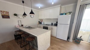 A modern kitchen with a central island, bar stools, a microwave, and a refrigerator.