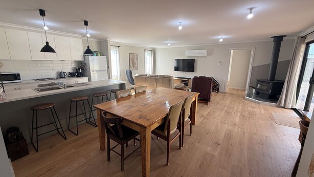 A modern kitchen with a central island, bar stools, a dining table, and a built-in stove.