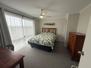 A bedroom with a bed, a ceiling fan, a dresser, and a window with curtains.