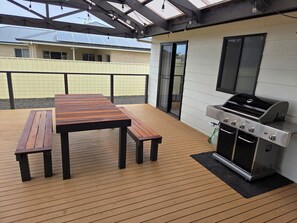 Eine Terrasse im Freien mit einem Holztisch, Bänken, einem Grill und einer Schiebetür.