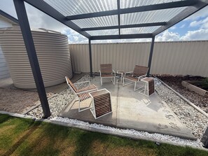 A covered patio area with outdoor seating, a large water tank, and a gravel pathway.