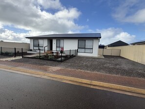 A single-story building with a flat roof, a fenced yard, and a gravel driveway.