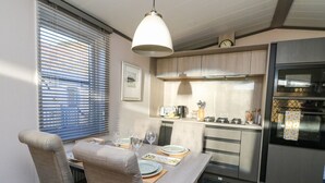 A modern kitchen with a dining area, featuring a table set for two, a hanging light fixture, and a built-in oven.