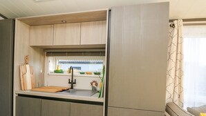 A compact kitchen with a built-in sink, wooden cabinets, and a window with a view.