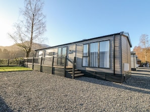 A single-story mobile home with a covered porch, large windows, and a gravel driveway.