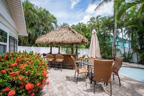 Eine Terrasse mit Korbmöbeln, einem Reetdachschirm und einem Pool.