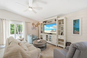 Ein Wohnzimmer mit Fernseher, einer Couch, einem Couchtisch und einem Deckenventilator.