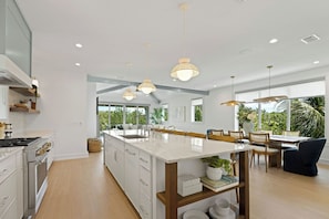 A modern kitchen with a large island, pendant lights, and a dining area with a view. - Hardin Hideaway - Anna Maria Island (Anna Maria)