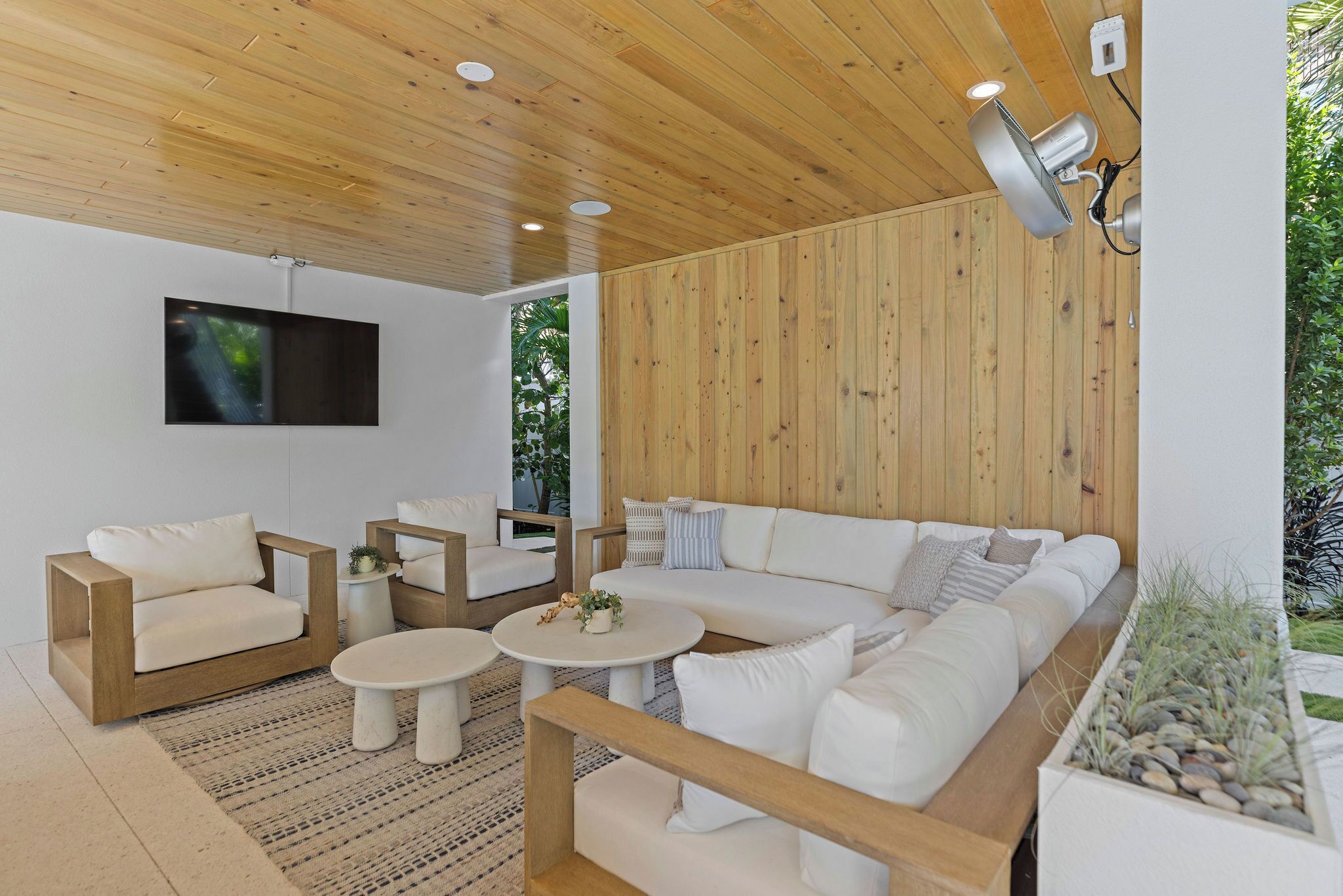 Un salon moderne avec un plafond en bois, des canapés blancs et un téléviseur à écran plat fixé au mur.