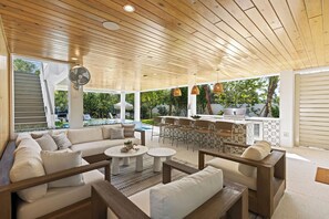 A covered outdoor seating area with a wooden ceiling, white sofas, round tables, and a bar area with wicker chairs. - Hardin Hideaway - Anna Maria Island (Anna Maria)