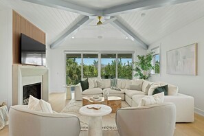 A spacious living room with a fireplace, large windows, and a ceiling fan. - Hardin Hideaway - Anna Maria Island (Anna Maria)