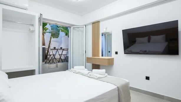 A modern hotel room with a bed, a mirror, a TV, and a view of a balcony with a plant.