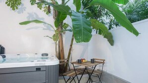 A hot tub with a wooden table and chairs, surrounded by large green plants.