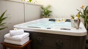 Ein Whirlpool mit zwei Gläsern Weißwein, ein Eimer mit Trauben und einer Flasche sowie ein Stapel weißer Handtücher auf einem Holzschemel.