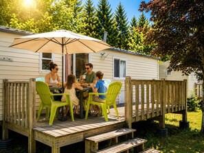 A family dining at a wooden deck with a table and chairs, a covered umbrella, and a view of a forested area.