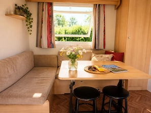 A cozy kitchenette with a wooden table, two stools, a vase with flowers, and a window with curtains.