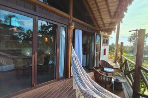A wooden deck with a hammock, wicker furniture, and large sliding glass doors overlooking a tropical landscape. - Serena Pousada Icaraí de Amontada (Amontada)