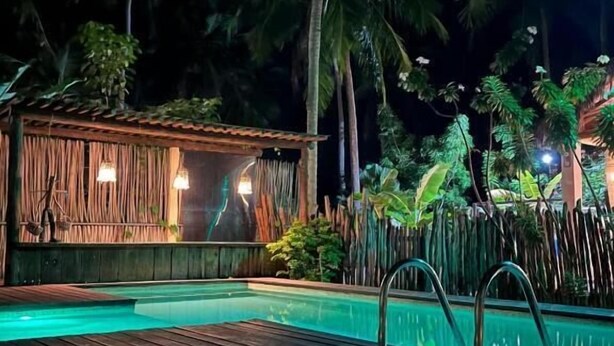 Una terraza de madera con piscina, rodeada de palmeras y una estructura de bambú.