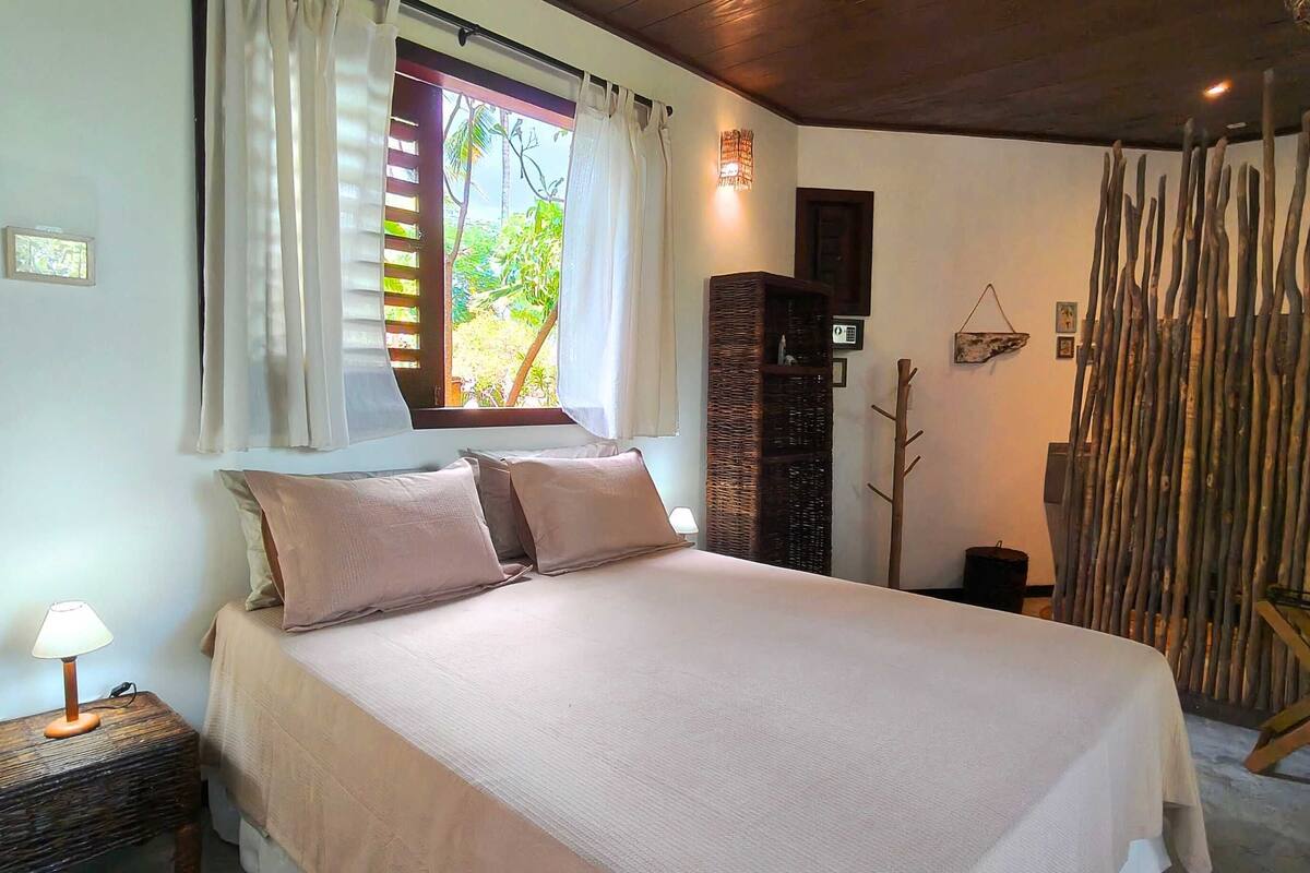 A bed with a headboard, a bedside lamp, a window with curtains, a wall-mounted shelf, and a decorative wall piece.