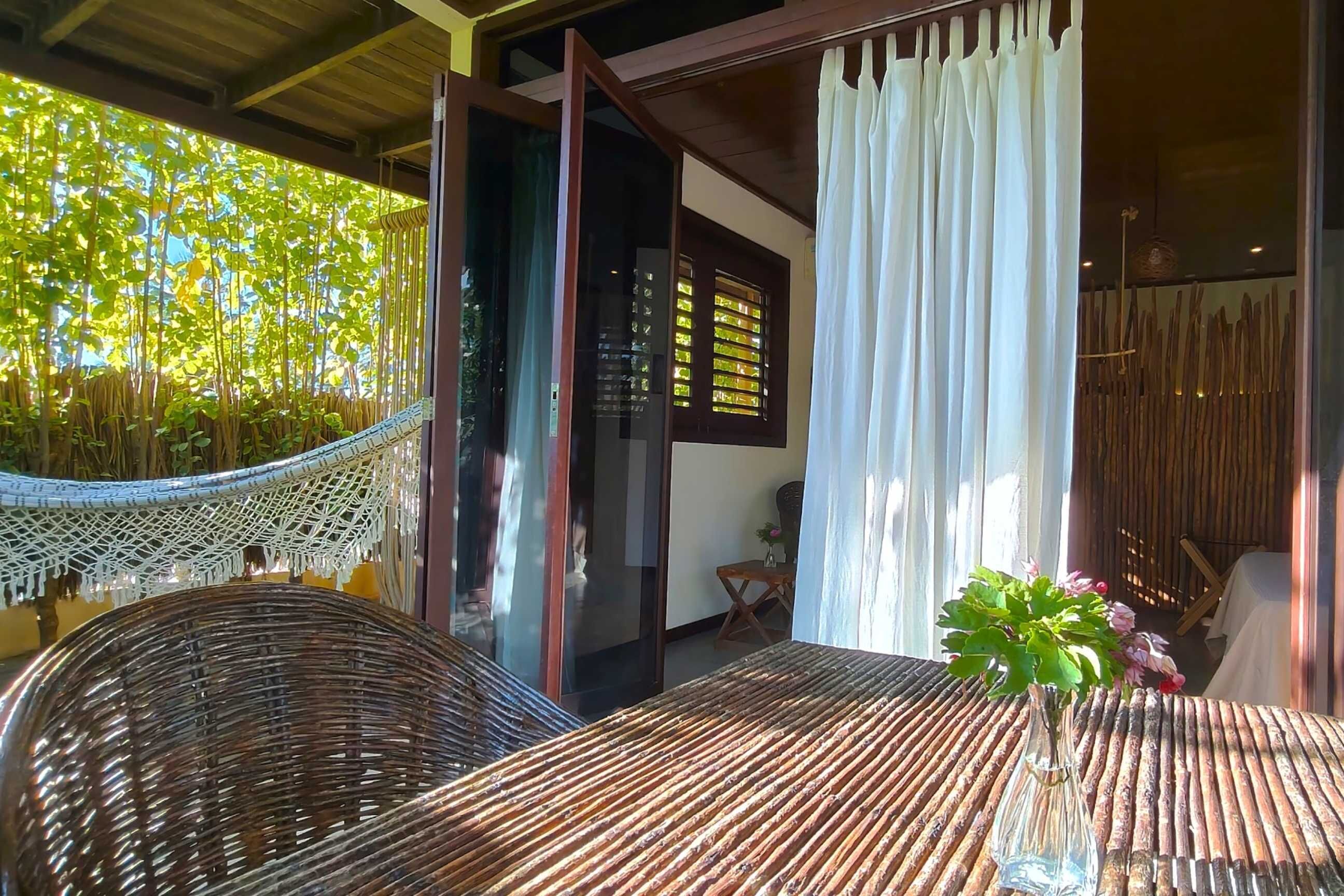 A room with a woven table, a hammock, and a view of greenery outside.