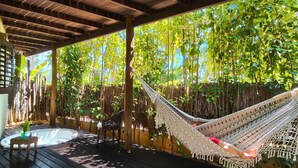 Una hamaca bajo una pérgola de madera, un jacuzzi y una mesa con sillas en una terraza de madera.