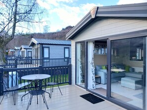 Ein modernes Haus mit Terrasse, einer Glasschiebetür zu einem Wohnbereich mit Sofa und Kissen sowie Blick auf die umliegende Landschaft.