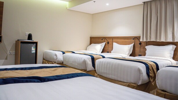 A hotel room with three beds, a wooden headboard, a small desk, and a window with curtains. - Rayan Al Jiwar Hotel (Makkah)