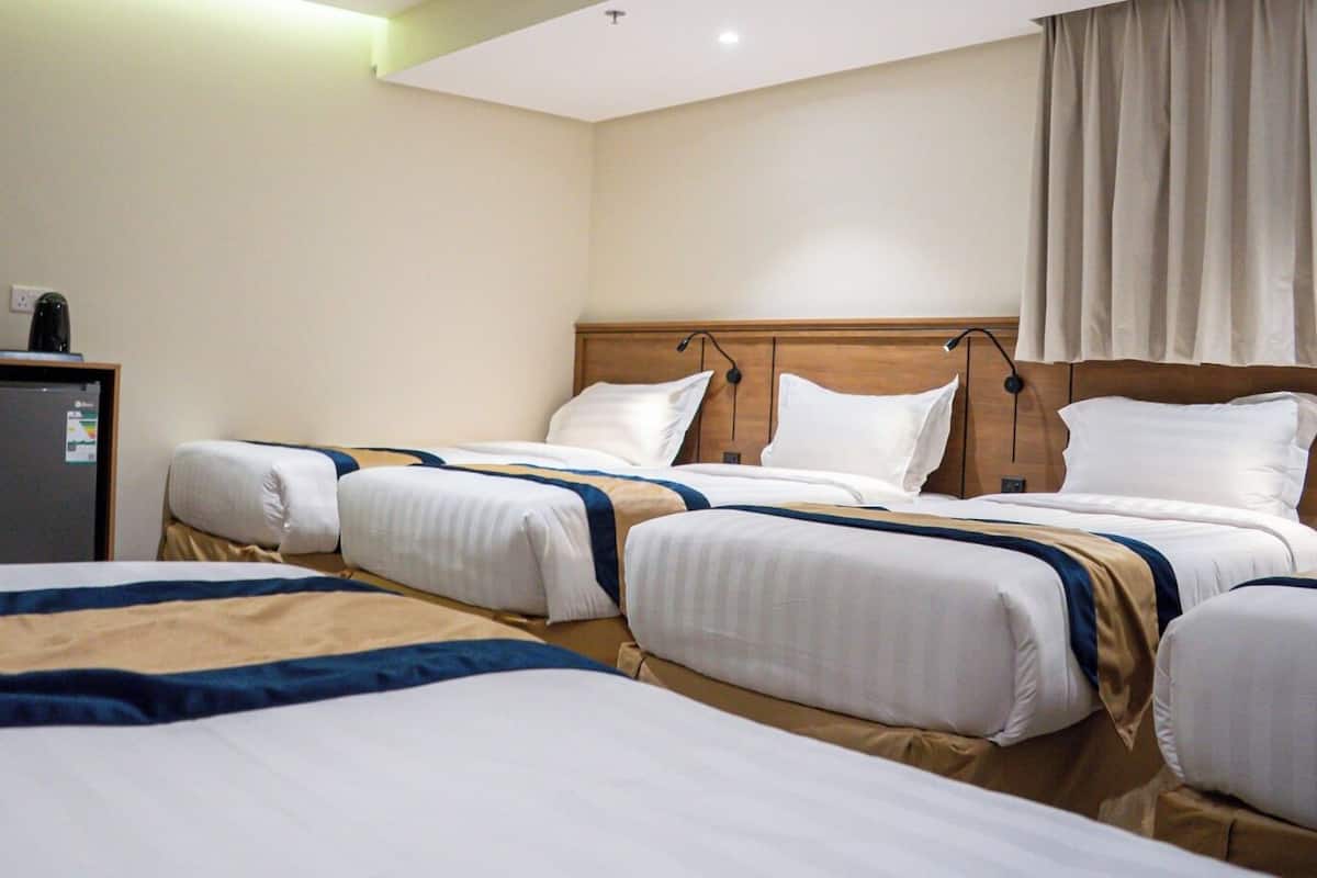 Habitación de hotel con tres camas, cabecera de madera, un escritorio pequeño y una ventana con cortinas.